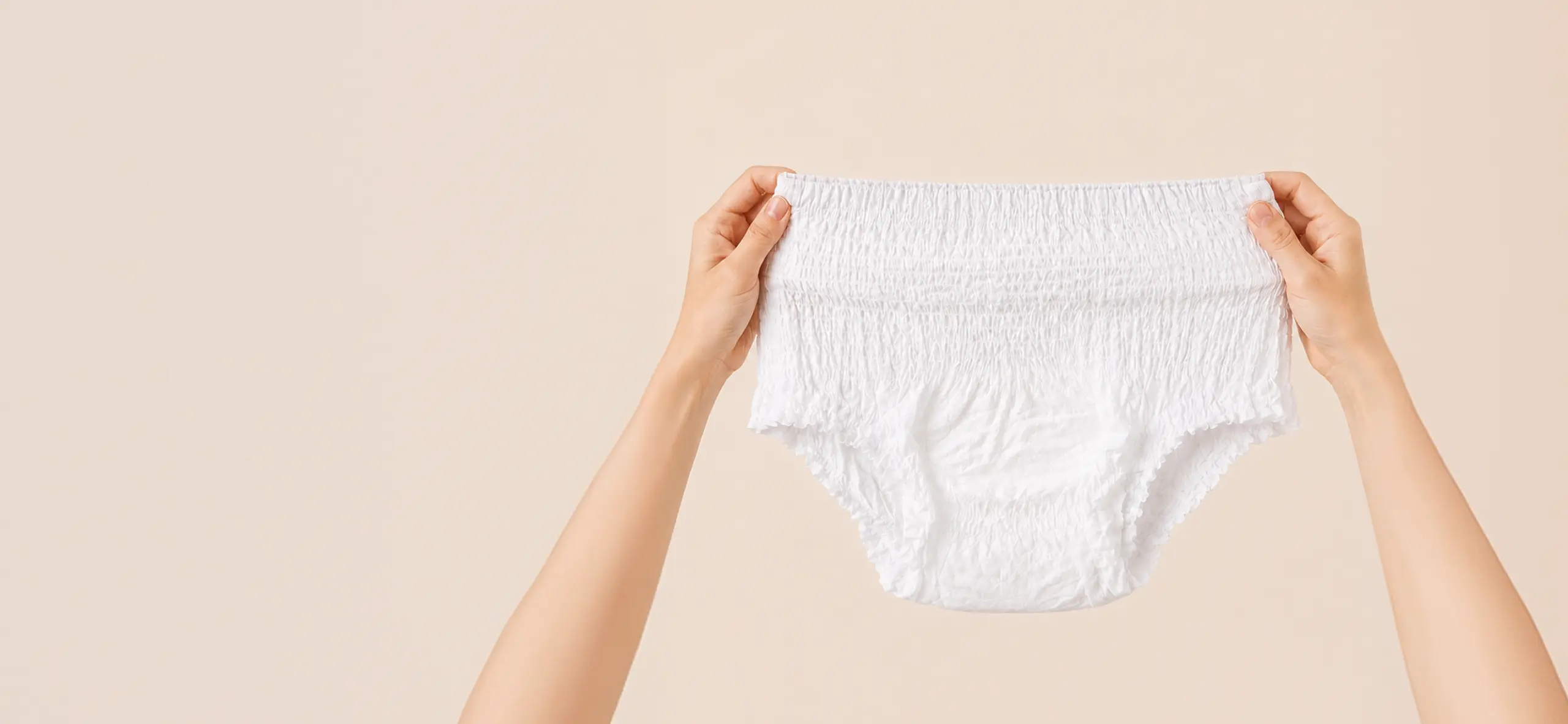 White pull-up continence underwear held by two hands against a soft neutral background.